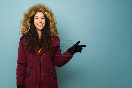 Téléchargez les photos : Latina belle jeune femme avec une veste d'hiver profiter de l'hiver froid pointant vers l'espace publicitaire copie bleue - en image libre de droit