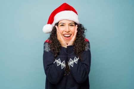 Photo for Surprised attractive young woman with a santa hat screaming with happiness celebrating the christmas holidays looking excited receiving good news - Royalty Free Image