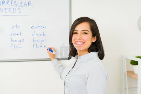 Téléchargez les photos : Heureuse femme attrayante souriante tout en écrivant sur le tableau blanc enseignant une leçon d'anglais à la classe - en image libre de droit