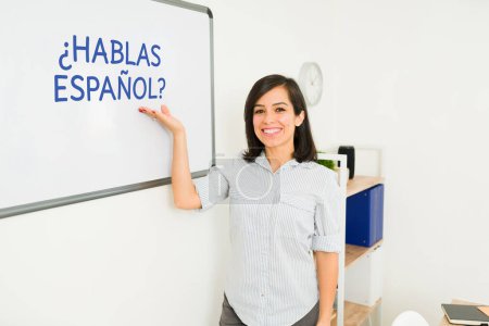 Téléchargez les photos : Professeur de langue étrangère caucasien excité souriant tout en pointant vers le conseil pendant les cours d'espagnol faire un contact visuel - en image libre de droit