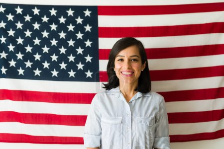 Foto de Patriota mujer caucásica en sus 30 años sonriendo mirando feliz de pie frente a la bandera de Estados Unidos emocionado por el sueño americano - Imagen libre de derechos