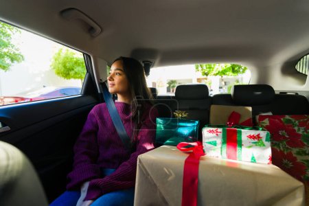 Téléchargez les photos : Femme hispanique souriante assise sur le siège arrière de la voiture tout en faisant du shopping en famille ou entre amis pour les cadeaux de Noël pendant les vacances - en image libre de droit