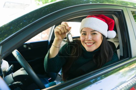 Foto de Retrato de una mujer atractiva de unos 30 años con un sombrero de santa que muestra las llaves después de comprar un coche nuevo para Navidad - Imagen libre de derechos
