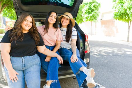 Foto de Retrato de un grupo de mujeres jóvenes y mejores amigos divirtiéndose juntos durante un viaje por carretera y sentados en el maletero del automóvil al aire libre - Imagen libre de derechos