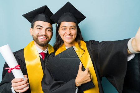 Foto de Mujer joven y feliz tomando una selfie con un atractivo hombre y amigo mientras celebran durante su graduación universitaria - Imagen libre de derechos
