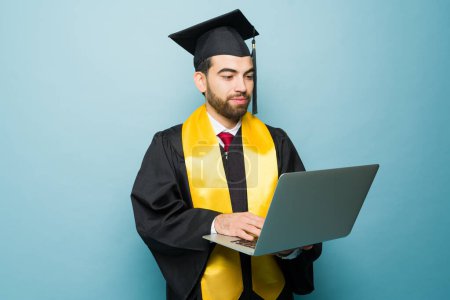Photo for Latin smart college student using the laptop receiving his university degree after studying online and receiving his diploma - Royalty Free Image