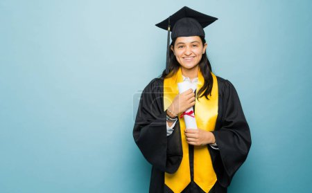 Foto de Mujer joven latina inteligente sonriendo sintiéndose orgullosa de terminar la universidad y recibir su diploma universitario con un vestido de graduación negro - Imagen libre de derechos