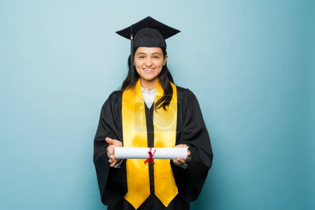 Foto de Retrato de una hermosa graduada feliz que se ve alegre y emocionada con su vestido de graduación después de recibir su diploma universitario - Imagen libre de derechos