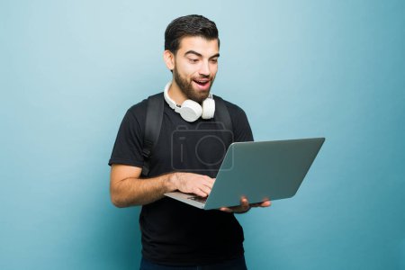 Photo for Handsome latin man student using the laptop and looking surprised and excited about the fast internet wifi in front of a studio background - Royalty Free Image