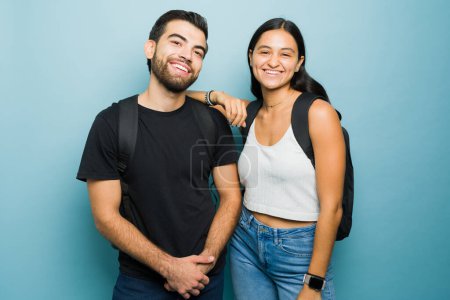 Foto de Retrato de atractiva pareja hispana feliz sonriendo llevando sus mochilas luciendo felices mientras estudian en la universidad - Imagen libre de derechos