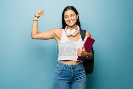 Téléchargez les photos : Forte jeune femme latine montrant son muscle biceps et sentant la puissance de la fille tout en étudiant l'université regardant heureux - en image libre de droit