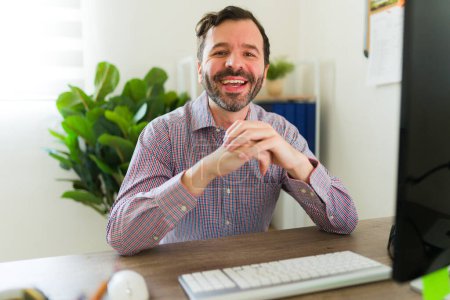 Photo for Excited attractive man boss and businessman smiling and enjoying working as a happy lawyer sitting at his desk in the office - Royalty Free Image