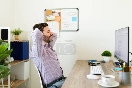 Photo for Hispanic happy man and boss relaxing while working at his office desk and smiling after finishing his work as a boss and entrepreneur - Royalty Free Image