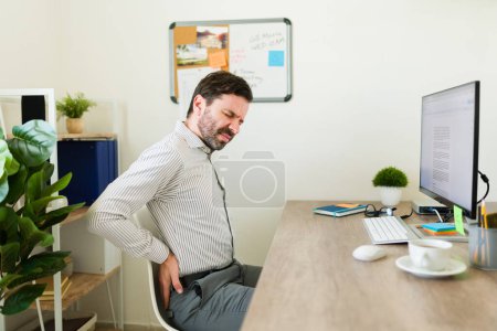 Photo for Tired lawyer or boss suffering back pain because of bad posture while sitting and working at his office desk - Royalty Free Image