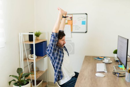 Foto de Hombre hispano activo haciendo ejercicio en el trabajo mientras está en la oficina haciendo ejercicios de entrenamiento frente al escritorio de la computadora - Imagen libre de derechos
