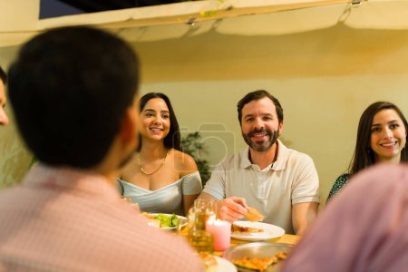 Téléchargez les photos : Hispanique heureux homme souriant parler lors d'un dîner amusant avec ses amis boire de la bière pour une célébration de l'amitié - en image libre de droit
