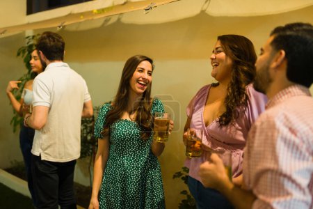 Téléchargez les photos : Joyeux beau groupe de personnes riant et s'amusant tout en buvant de la bière lors d'une fête la nuit dans la cour arrière - en image libre de droit