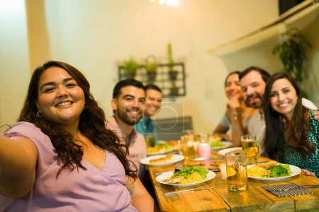 Téléchargez les photos : Point de vue personnel d'un groupe de jeunes assis à la table prêts à dîner ensemble lors d'une célébration amusante prenant un selfie - en image libre de droit