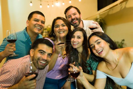 Téléchargez les photos : Groupe heureux de femmes et d'hommes qui s'amusent à boire du vin pour une célébration après le dîner avec des amis qui rient et sourient - en image libre de droit