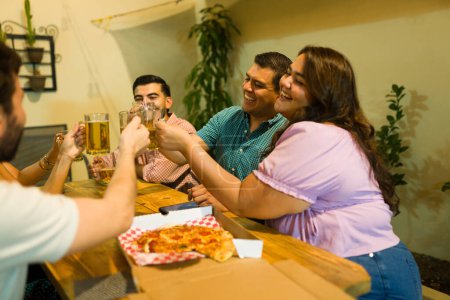Téléchargez les photos : Groupe attrayant d'amis s'amuser à rire tout en faisant un toast boire de la bière et profiter de manger de la pizza - en image libre de droit