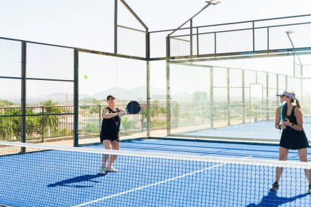 Téléchargez les photos : Équipe de femmes caucasiennes jouant un match de sport à l'aide de raquettes et de tennis padel d'entraînement regardant heureux - en image libre de droit