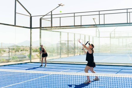 Foto de Hermosas mujeres entrenando en equipo al aire libre en la cancha de tenis y jugando un partido de padel divirtiéndose - Imagen libre de derechos