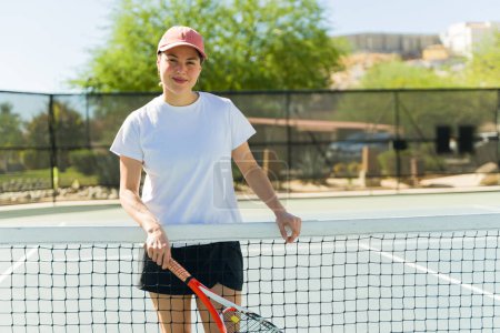 Foto de Atractiva mujer caucásica disfrutando practicando tenis usando una raqueta y sonriendo en la cancha al aire libre - Imagen libre de derechos