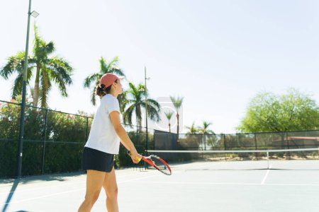 Foto de Vista trasera de una joven feliz entrenando y practicando su servicio de tenis usando una raqueta en la cancha de tenis - Imagen libre de derechos