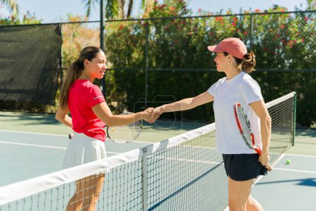 Foto de Mujeres hermosas activas estrechando la mano y celebrando después de un buen partido de tenis en la cancha de tenis al aire libre - Imagen libre de derechos