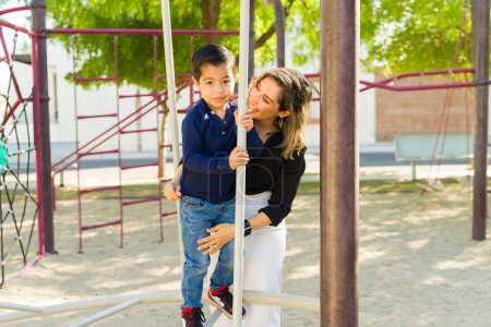 Téléchargez les photos : Joyeux beau maman souriant avec son adorable petit garçon jouant dans le parc et s'amusant ensemble à l'aire de jeux - en image libre de droit
