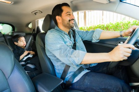 Téléchargez les photos : Attrayant père heureux conduisant son petit garçon assis sur le siège d'appoint à la classe de karaté tout en souriant conduire la voiture - en image libre de droit