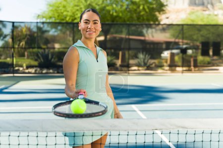 Foto de Feliz mujer latina atractiva jugando con una pelota de tenis y raqueta antes de comenzar un partido - Imagen libre de derechos