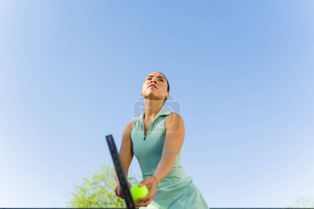 Téléchargez les photos : Angle bas d'une belle jeune femme latine utilisant une raquette et s'amusant à jouer à un match de tennis - en image libre de droit