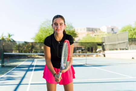 Téléchargez les photos : Joyeux belle adolescente avec une jupe rose souriant tout en apprenant à jouer au tennis et en s'amusant - en image libre de droit