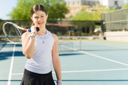 Photo for Adorable happy teen girl smiling holding a racket on the tennis court ready to practice during a tennis game - Royalty Free Image