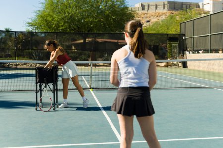 Téléchargez les photos : Adolescente active vue de derrière prenant des cours de tennis avec une entraîneuse sportive sur le court de tennis en plein air - en image libre de droit