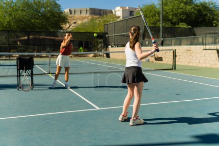 Téléchargez les photos : Coach femme sportive jetant une balle de tennis à une adolescente caucasienne prenant des cours de tennis en plein air - en image libre de droit