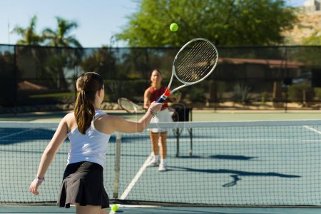 Téléchargez les photos : Belle adolescente pratiquant son coup droit en utilisant une raquette tout en prenant des cours de tennis avec un entraîneur - en image libre de droit