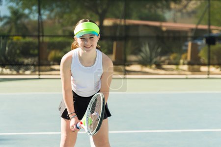 Téléchargez les photos : Joyeux joyeux adolescent fille souriant faire contact visuel tout en s'amusant à jouer à un jeu de tennis - en image libre de droit