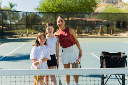 Téléchargez les photos : Hispanique femme entraîneur et son adolescent élèves souriant tout en prenant des cours de tennis avoir plaisir à regarder heureux - en image libre de droit