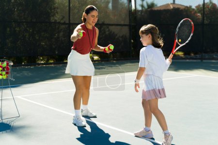 Téléchargez les photos : Belle femme entraîneur de tennis donnant des leçons à une fille caucasienne adorable caucasienne sur le court de tennis - en image libre de droit