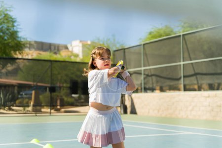 Téléchargez les photos : Belle fille sportive enfant jouer à un jeu de tennis amusant tout en prenant des leçons regardant heureux sur le court de tennis - en image libre de droit