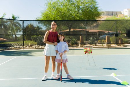 Téléchargez les photos : Happy femme latine entraîneur avec une étudiante caucasienne sportive apprenant à jouer au tennis et souriant - en image libre de droit