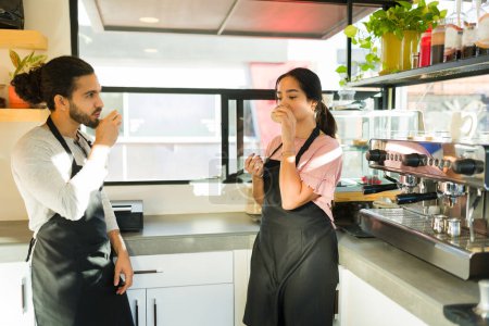 Photo for Hispanic couple of young baristas with aprons working at the cafe and drinking espresso coffee - Royalty Free Image
