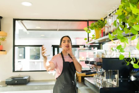 Téléchargez les photos : Belle femme latine et barista appelant le nom d'un client tout en distribuant un café pour aller au café - en image libre de droit