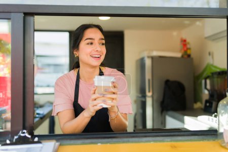 Photo for Excited beautiful young woman working as a barista and handing the coffee to-go to a customer smiling looking happy - Royalty Free Image