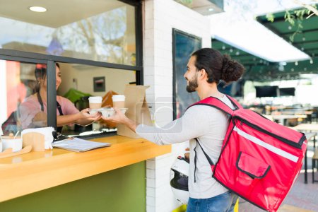 Photo for Happy man and delivery person smiling to the barista worker at the cafe while receiving the coffee and food to-go - Royalty Free Image