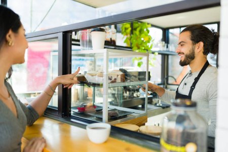 Téléchargez les photos : Gai mâle barista parler à un heureux client féminin achat dessert et café au café - en image libre de droit