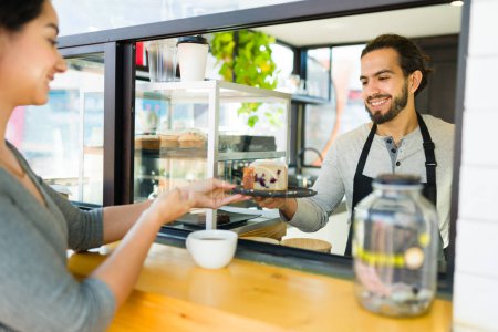 Téléchargez les photos : Attrayant mâle barista souriant remettre une pâtisserie de dessert à une cliente heureuse au café - en image libre de droit