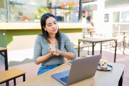 Photo for Latin young woman with headphones talking during an online video call using her laptop in the coffee shop - Royalty Free Image